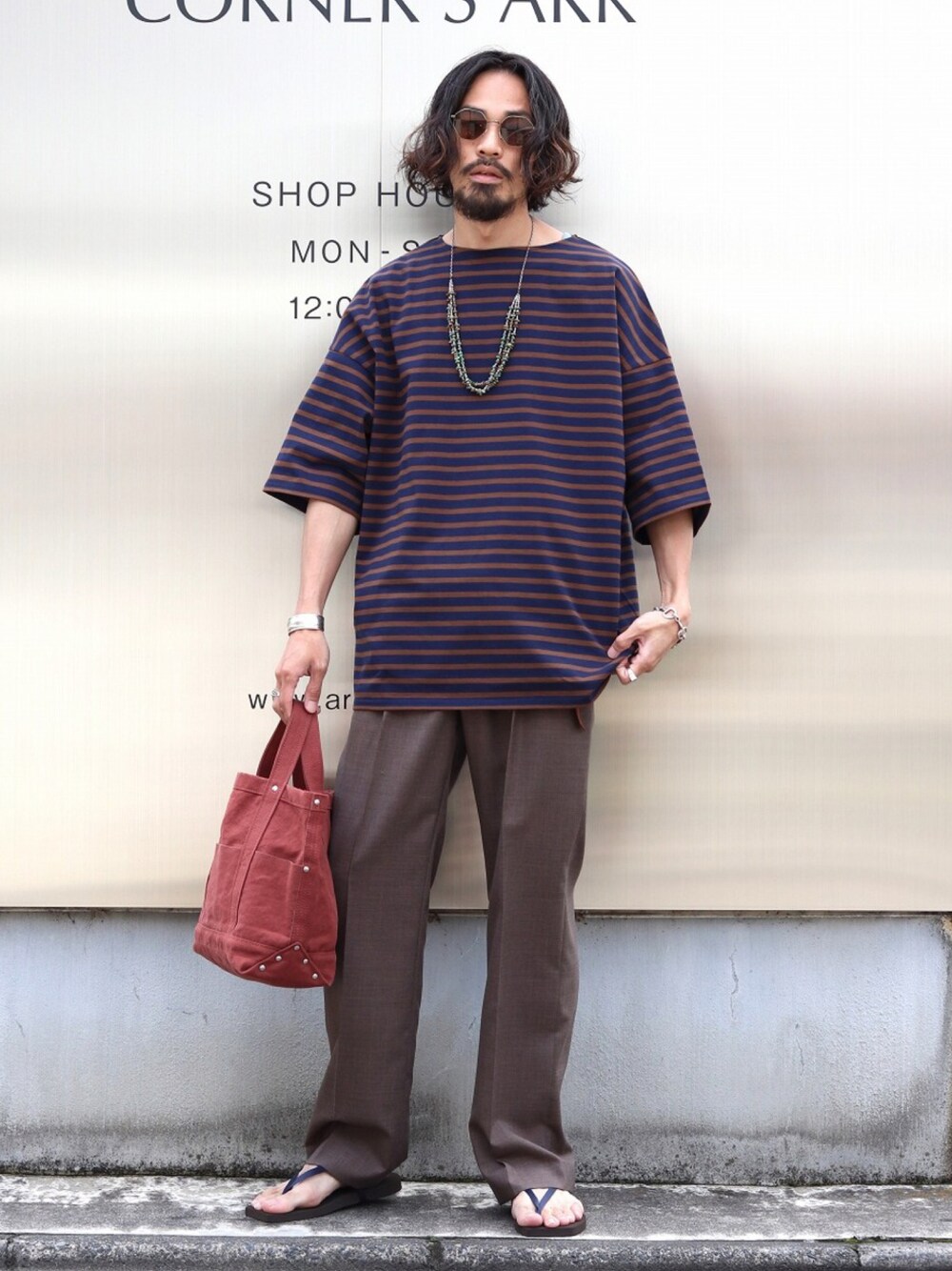 ブルー系のTシャツ/カットソー、ブラウン系のスラックス、レッド系のトートバッグを着用したメンズの夏コーディネートの1枚目の写真