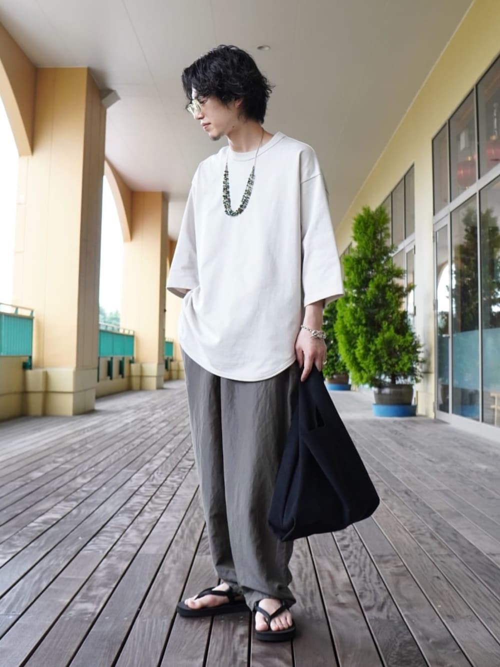 ホワイト系のTシャツ/カットソー、グレー系のスラックス、ブラック系のトートバッグを着用したメンズの夏コーディネートの1枚目の写真