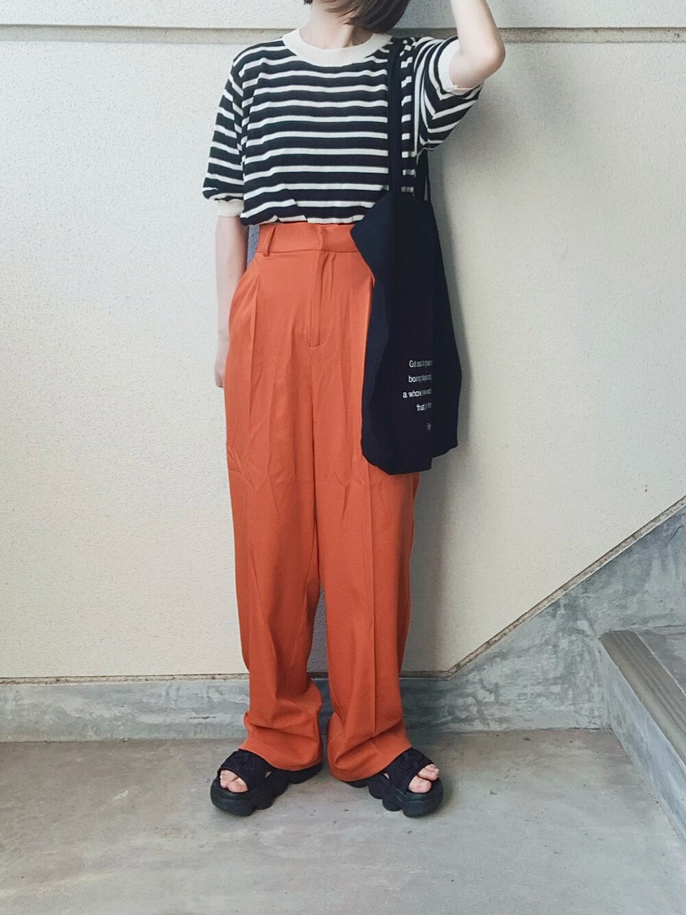 オレンジ系のスラックス、ブラック系のニット/セーター、ブラック系のトートバッグを着用したレディースの夏コーディネートの1枚目の写真