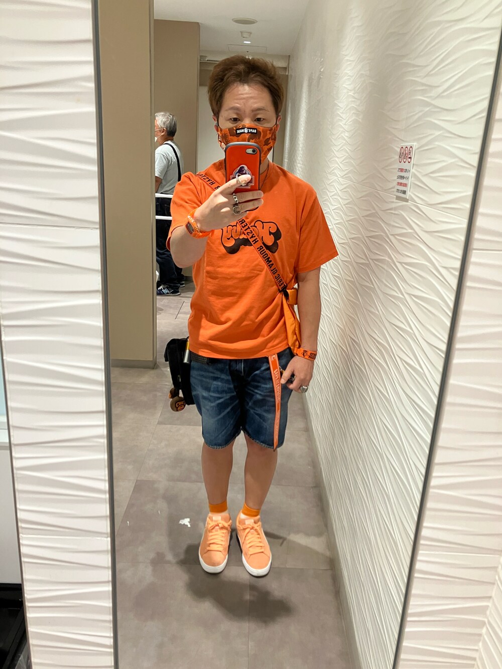 オレンジ系のTシャツ/カットソー、オレンジ系のトートバッグ、ブルー系のデニムパンツを着用したメンズの秋コーディネートの1枚目の写真