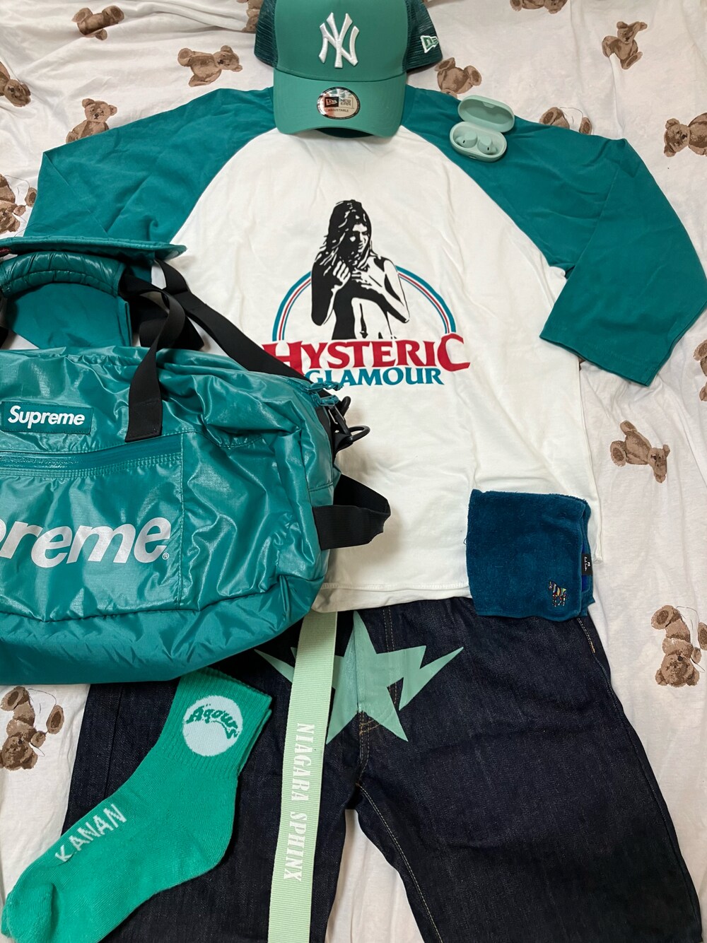グリーン系のTシャツ/カットソー、グリーン系のドラムバッグ、ブルー系のデニムパンツを着用したメンズの夏コーディネートの1枚目の写真