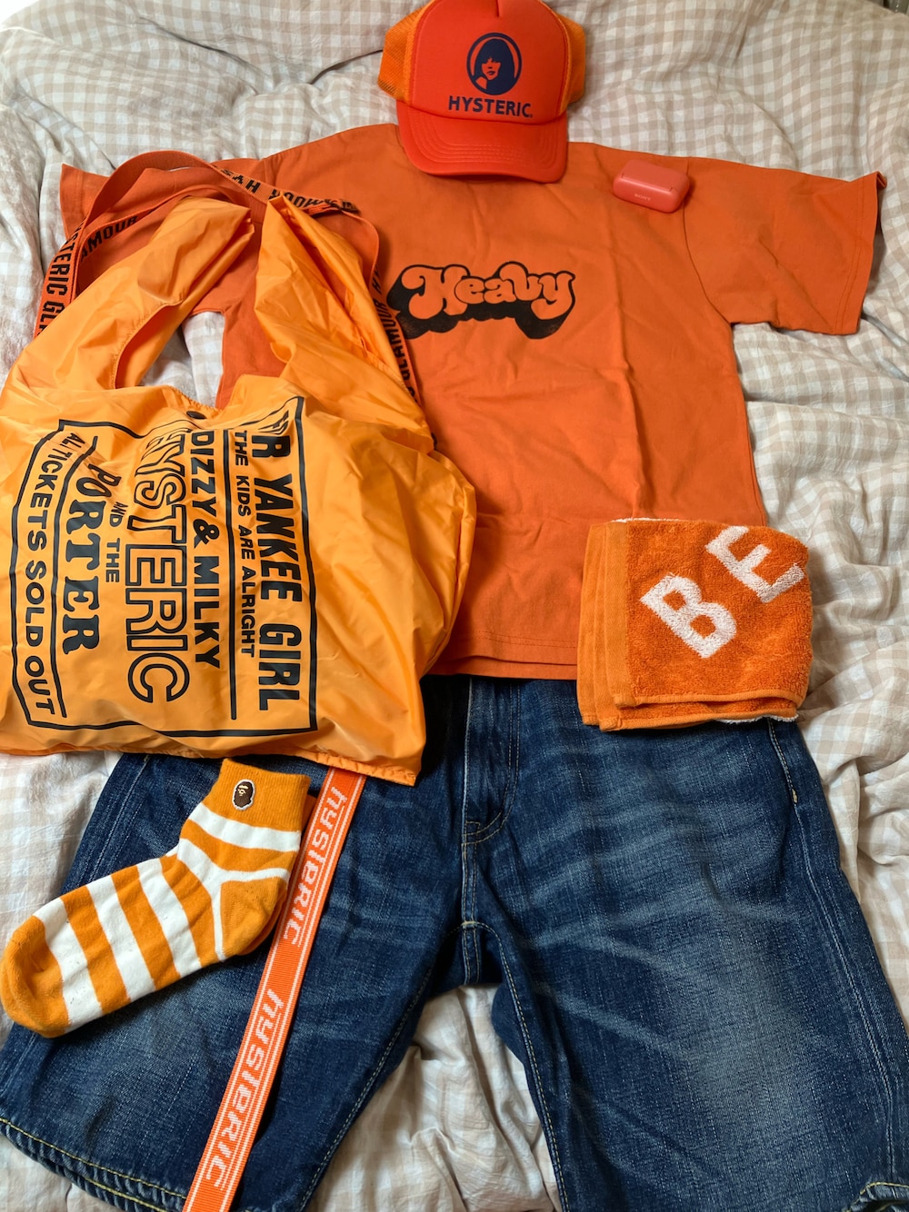 オレンジ系のTシャツ/カットソー、オレンジ系のトートバッグ、ブルー系のデニムパンツを着用したメンズの秋コーディネートの1枚目の写真