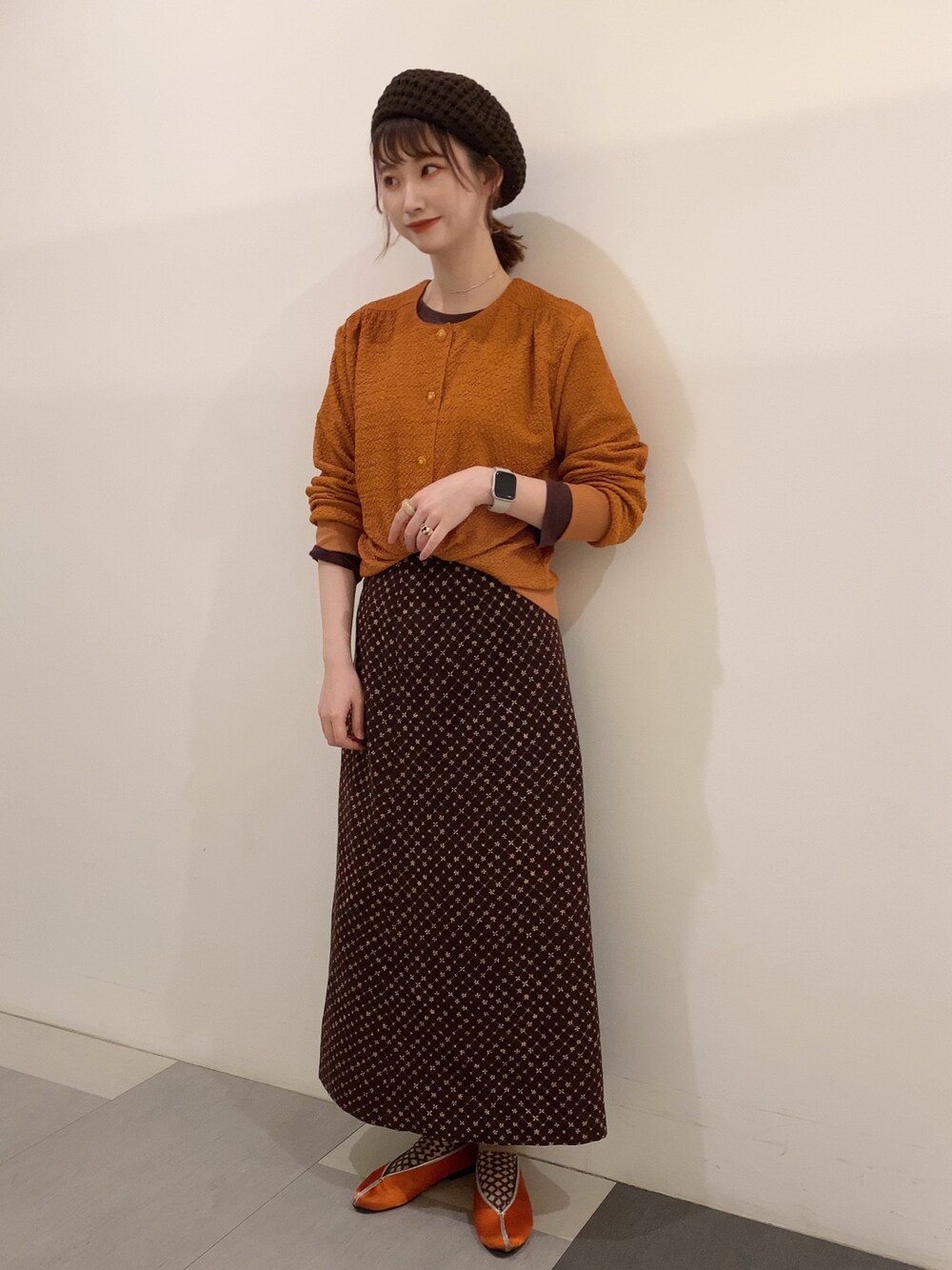 オレンジ系のカーディガン/ボレロ、ブラウン系のスカート、オレンジ系のシューズを着用したレディースの春コーディネートの2枚目の写真