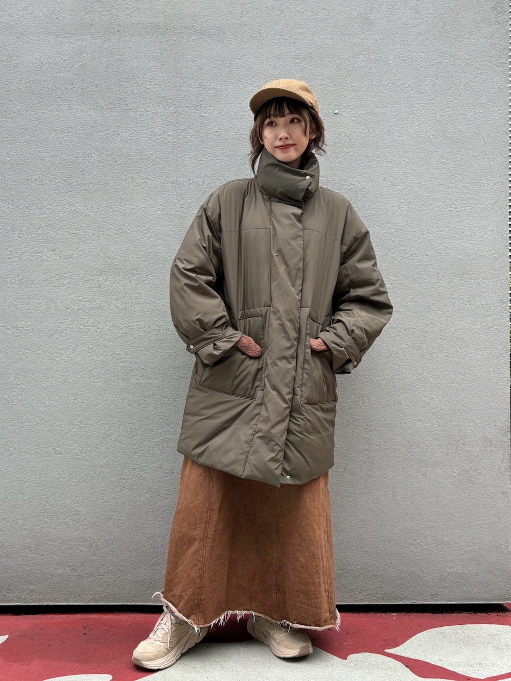 グリーン系のダウンジャケット/コート、ブラウン系のデニムスカート、ベージュ系のスニーカーを着用したレディースの秋コーディネートの1枚目の写真