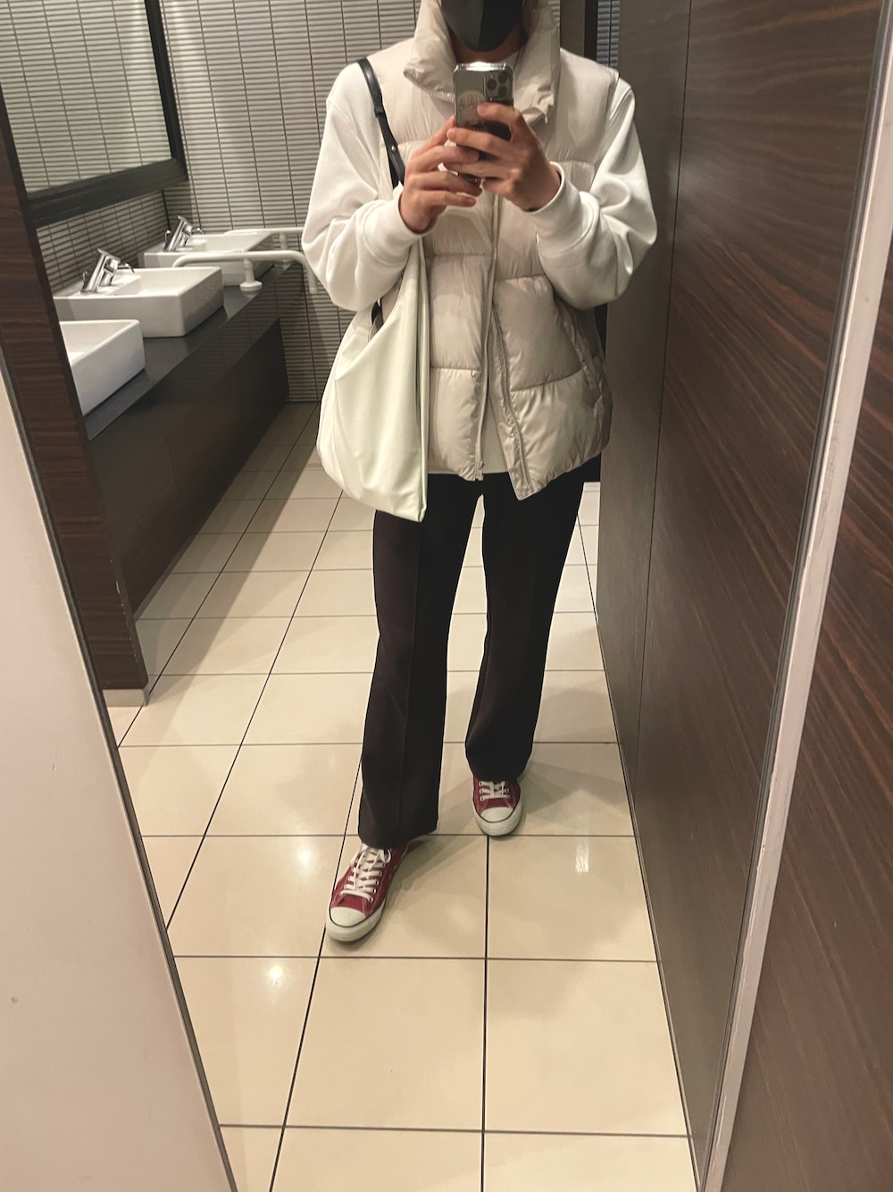 ホワイト系のダウンベスト、ブラウン系のスウェットパンツ、レッド系のスニーカーを着用したメンズの冬コーディネートの1枚目の写真