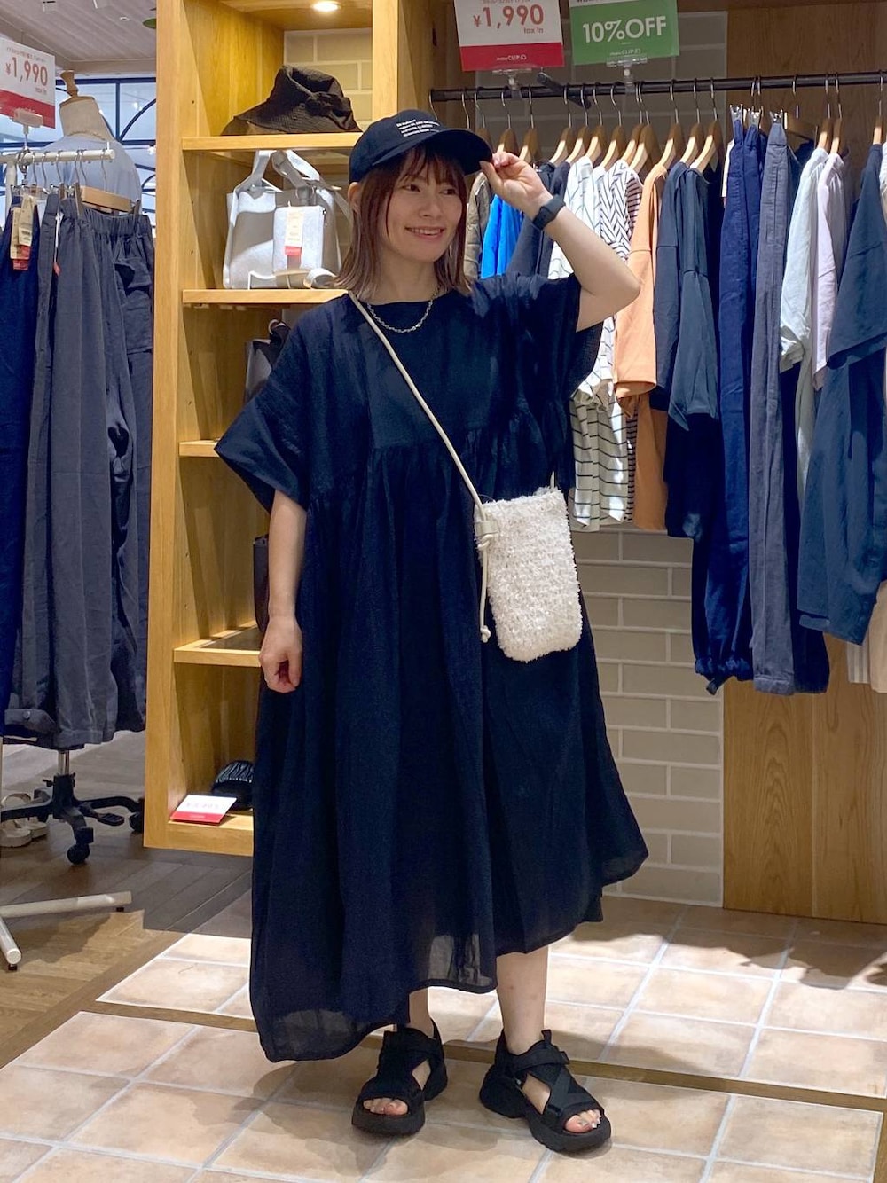 ホワイト系のショルダーバッグ、ブラック系のワンピース、ブラック系のサンダルを着用したレディースの夏コーディネートの1枚目の写真