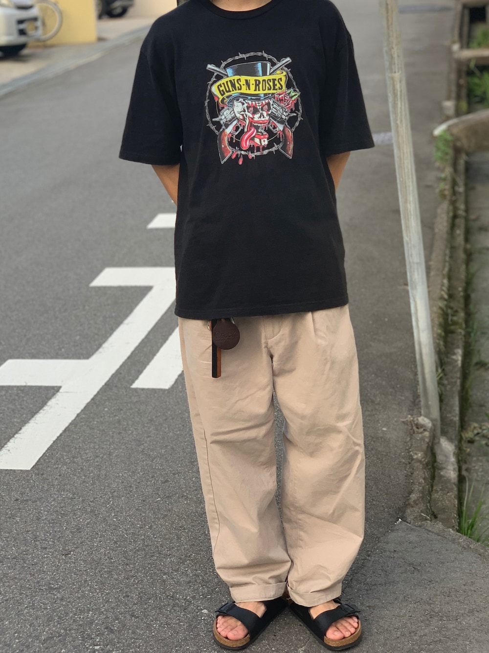 ベージュ系のチノパンツ、ブラック系のサンダル、ブラック系のTシャツ/カットソーを着用したメンズの夏コーディネートの1枚目の写真