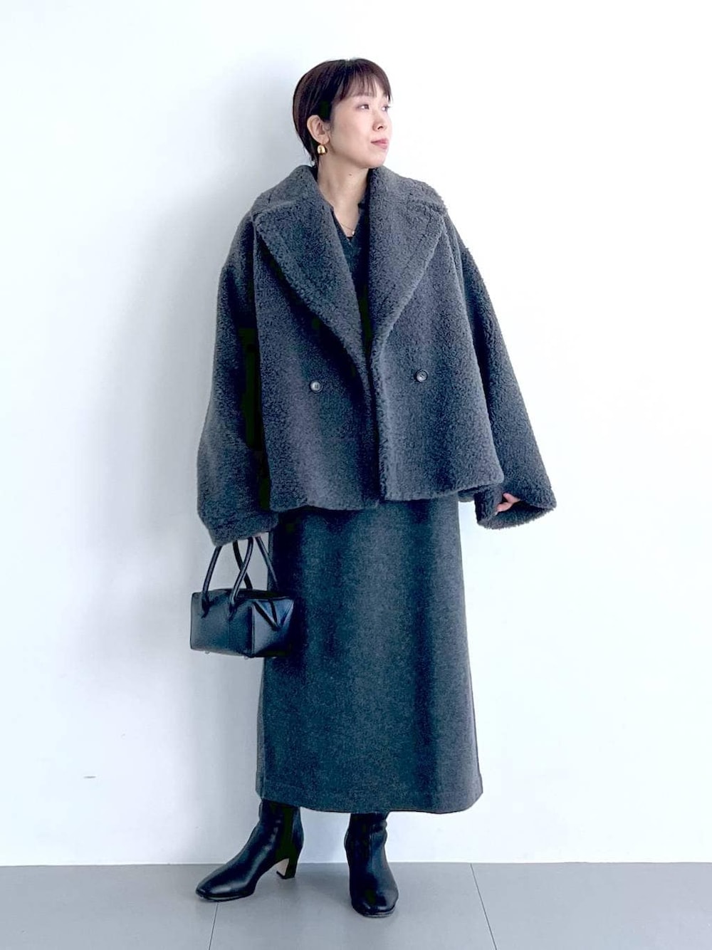 グレー系のピーコート、ブラック系のハンドバッグ、ブラック系のブーツを着用したレディースの秋コーディネートの1枚目の写真