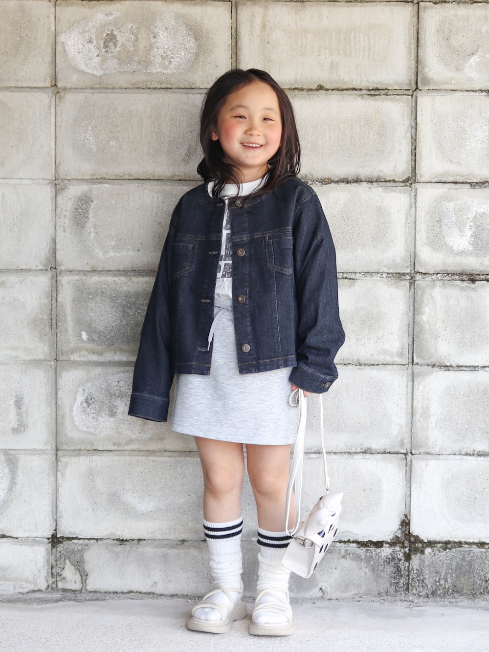 ブルー系のブルゾン、ホワイト系のワンピース、ホワイト系のショルダーバッグを着用したキッズの春コーディネートの1枚目の写真