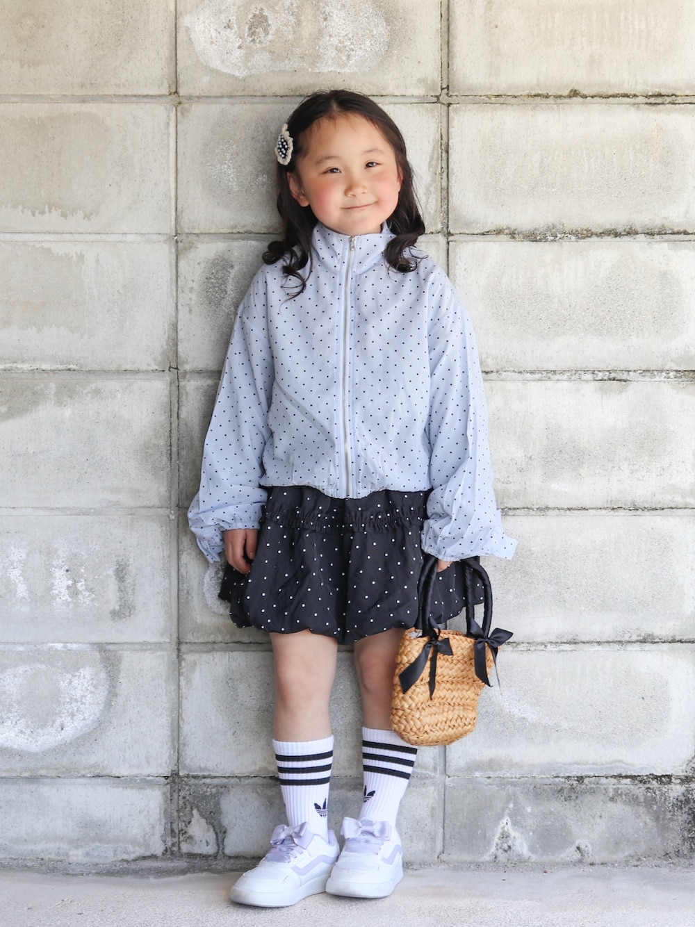 ブルー系のナイロンジャケット、ブラック系のスカート、ブラック系のかごバッグを着用したキッズの春コーディネートの1枚目の写真