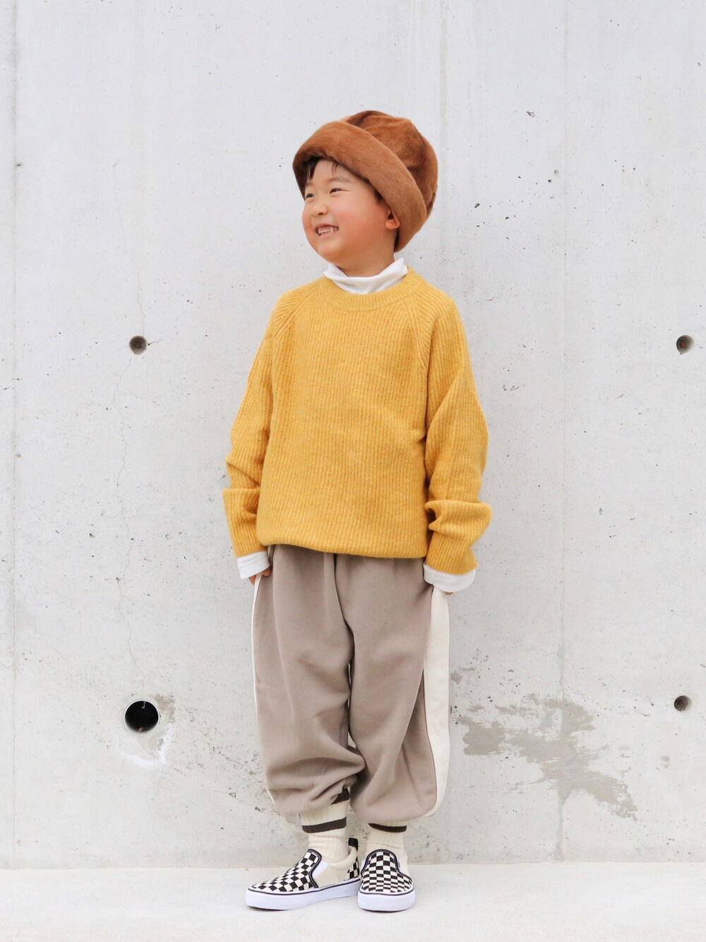イエロー系のニット/セーター、ホワイト系のTシャツ/カットソー、ブラウン系のパンツを着用したキッズの冬コーディネートの1枚目の写真