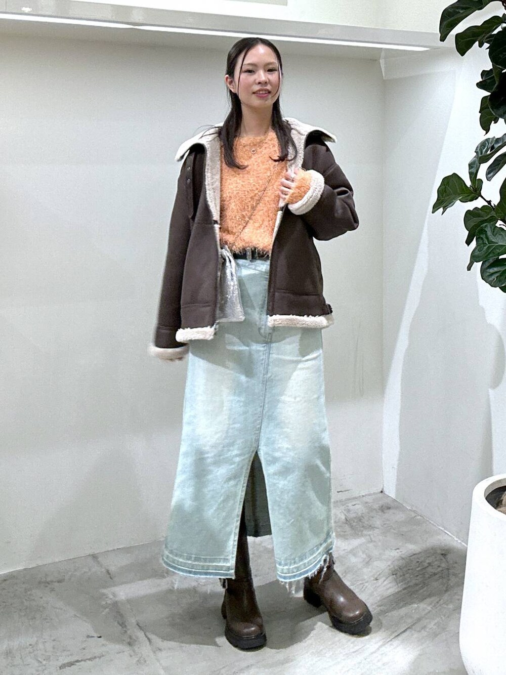 ブルー系のデニムスカート、ブラウン系のブーツ、シルバー系のショルダーバッグを着用したレディースの冬コーディネートの1枚目の写真