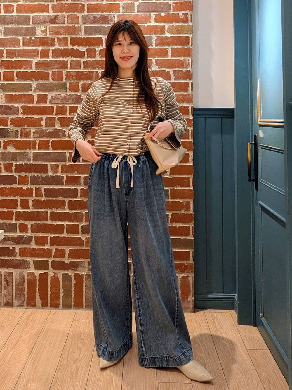 ブルー系のデニムパンツ、ベージュ系のショルダーバッグ、ホワイト系のパンプスを着用したレディースの春コーディネートの1枚目の写真