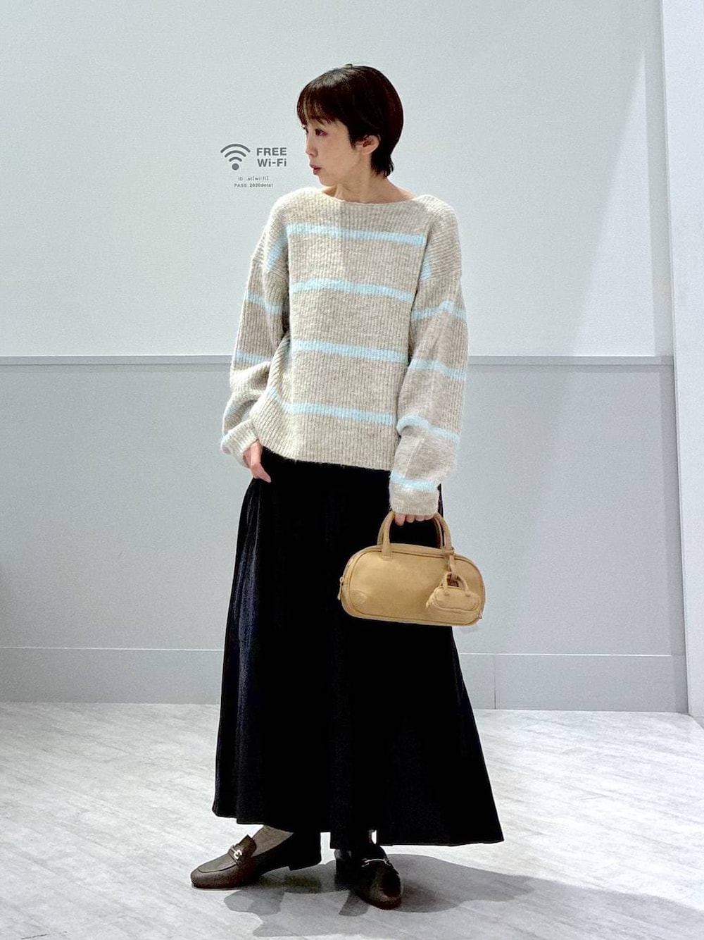 ベージュ系のローファー、グレー系のスカート、ブラウン系のハンドバッグを着用したレディースの秋コーディネートの1枚目の写真