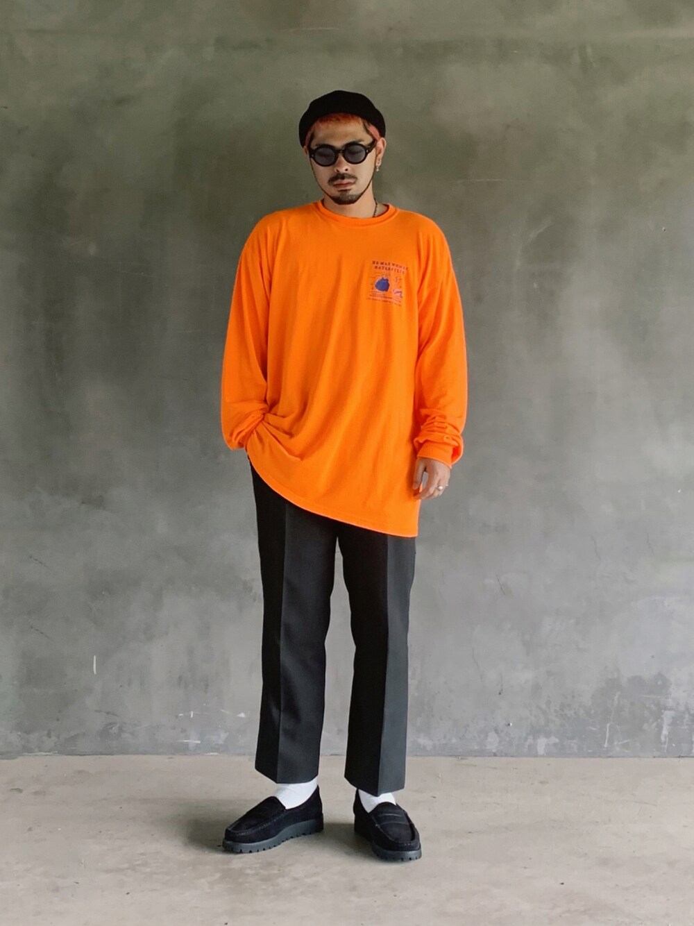 グレー系のスラックス、オレンジ系のTシャツ/カットソー、ブラック系のローファーを着用したメンズの秋コーディネートの1枚目の写真