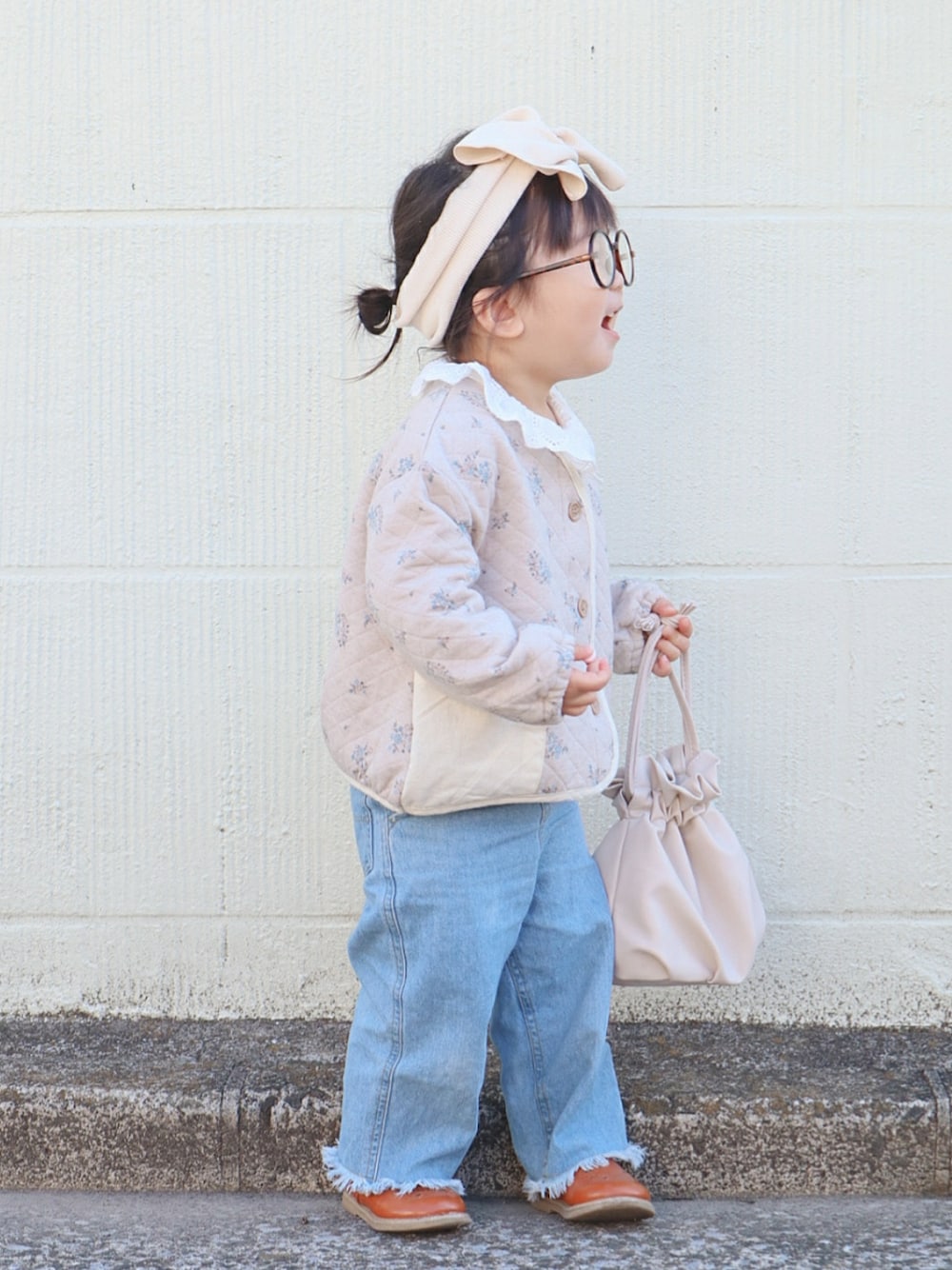ベージュ系のノーカラージャケット、ホワイト系のトートバッグ、ブルー系のデニムパンツを着用したキッズの春コーディネートの2枚目の写真