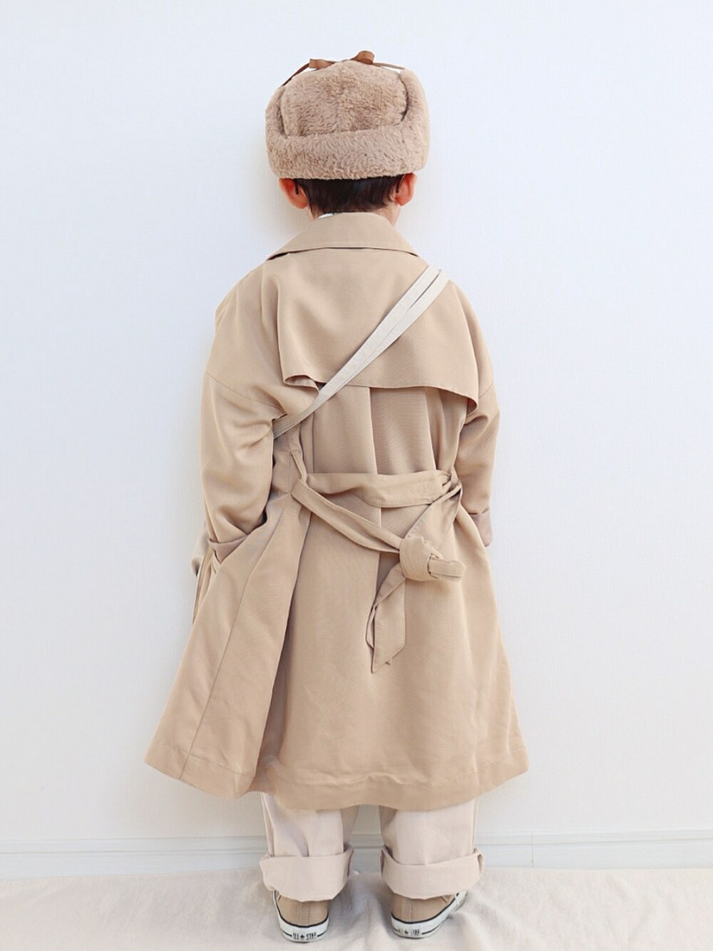 ベージュ系のトレンチコート、ホワイト系のニット/セーター、ホワイト系のトートバッグを着用したキッズの冬コーディネートの3枚目の写真