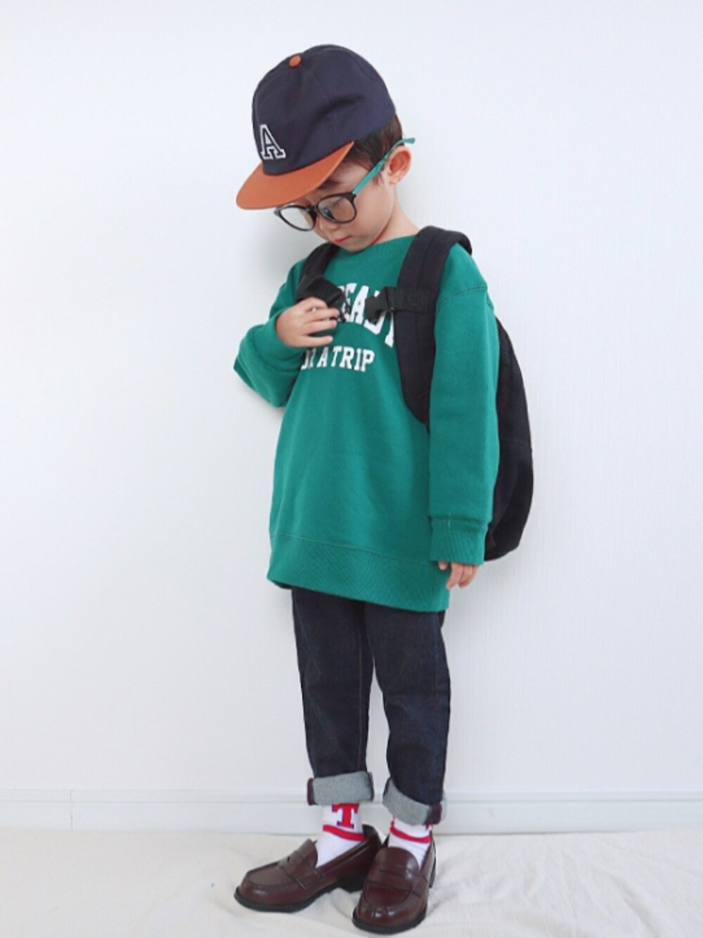 グリーン系のスウェット、ブラック系のバックパック/リュック、ブルー系のデニムパンツを着用したキッズの秋コーディネートの1枚目の写真