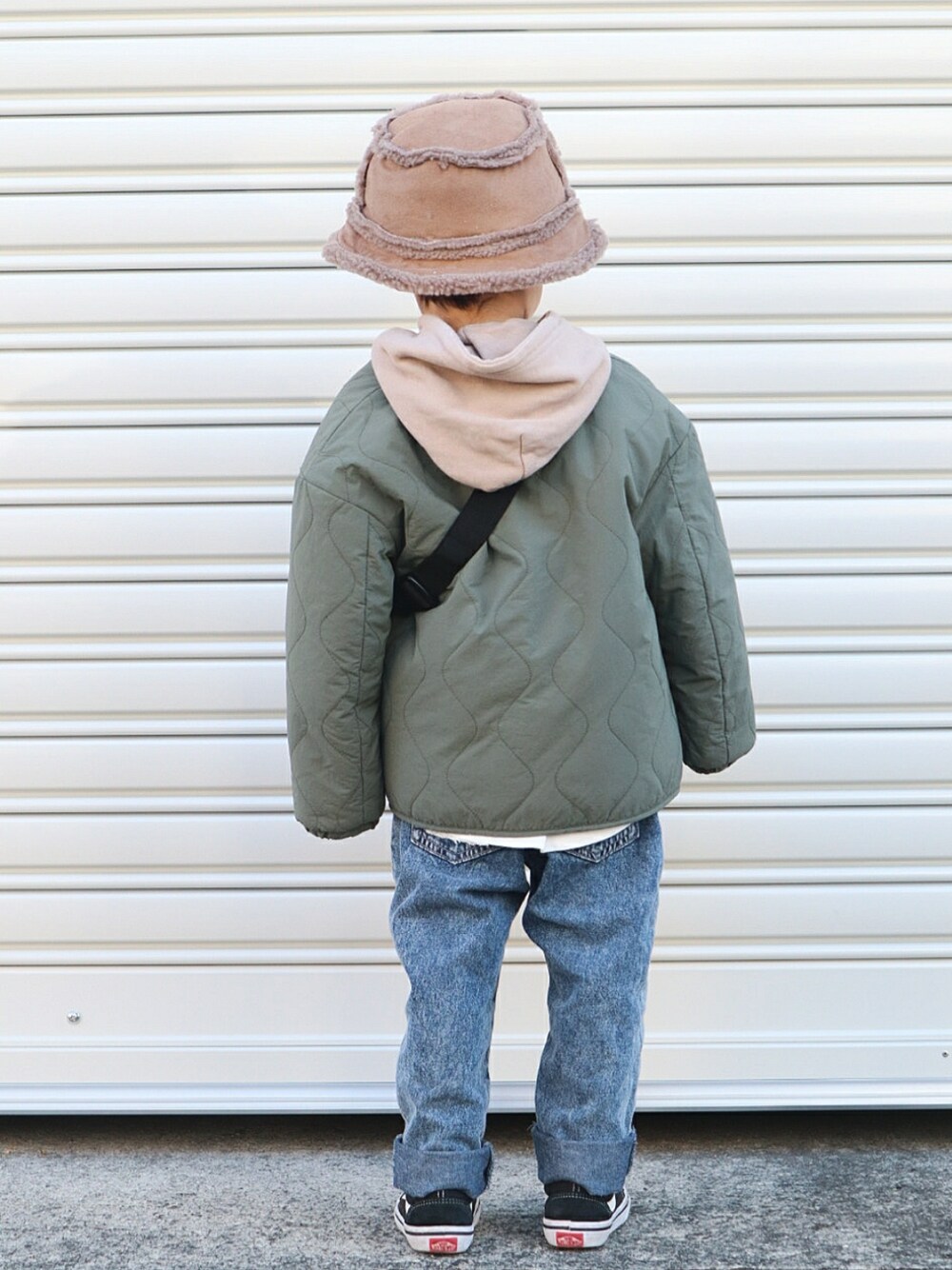 グリーン系のノーカラーコート、ベージュ系のパーカー、ブルー系のデニムパンツを着用したキッズの冬コーディネートの2枚目の写真