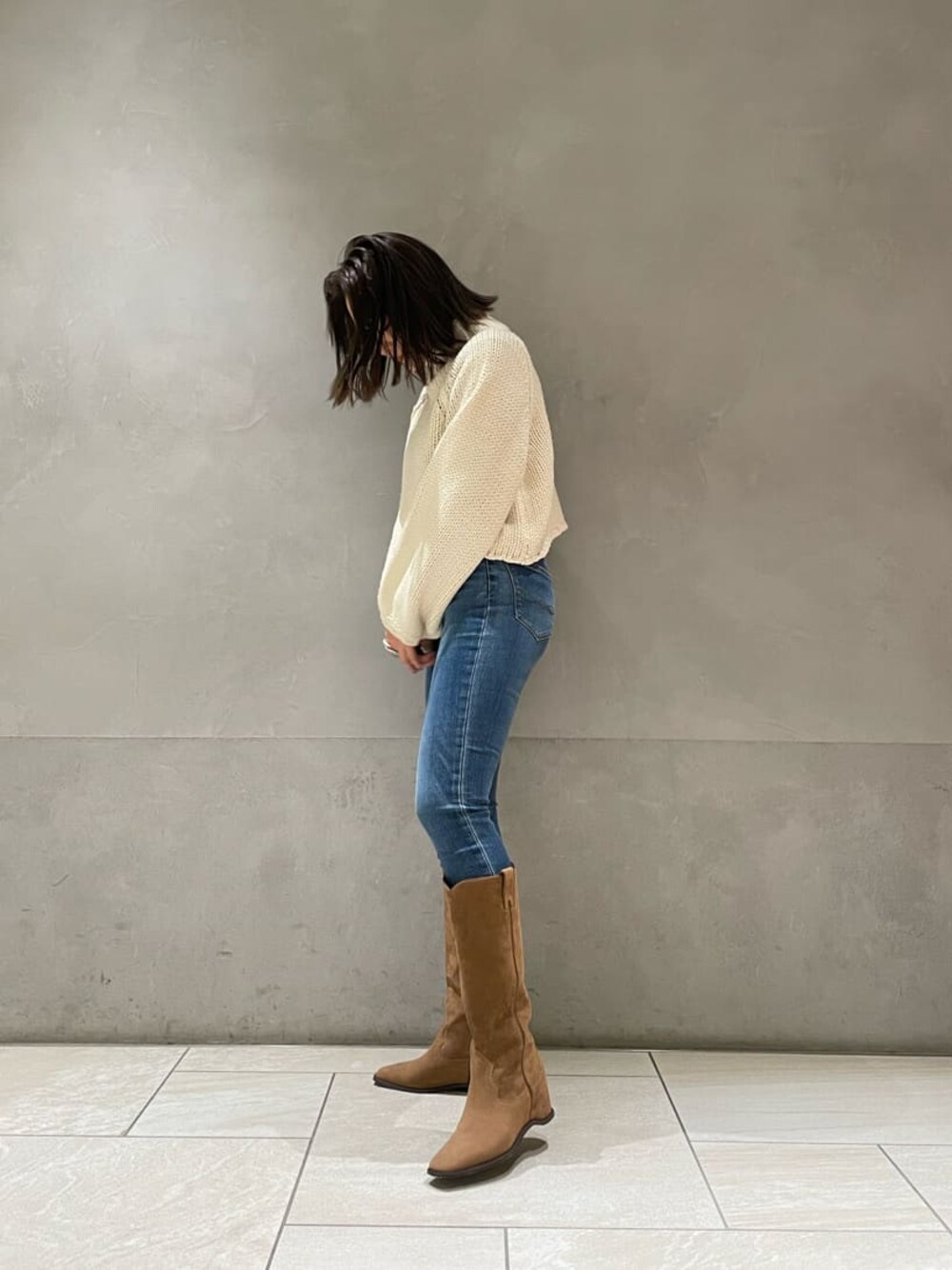 ベージュ系のブーツ、ホワイト系のニット/セーター、ブルー系のデニムパンツを着用したレディースの秋コーディネートの1枚目の写真