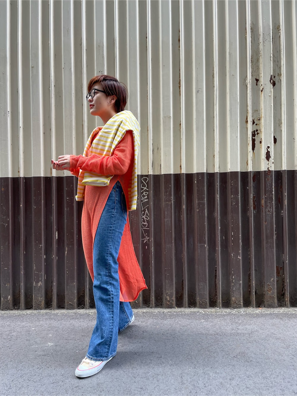 ブルー系のデニムパンツ、オレンジ系のワンピースを着用したレディースの春コーディネートの1枚目の写真