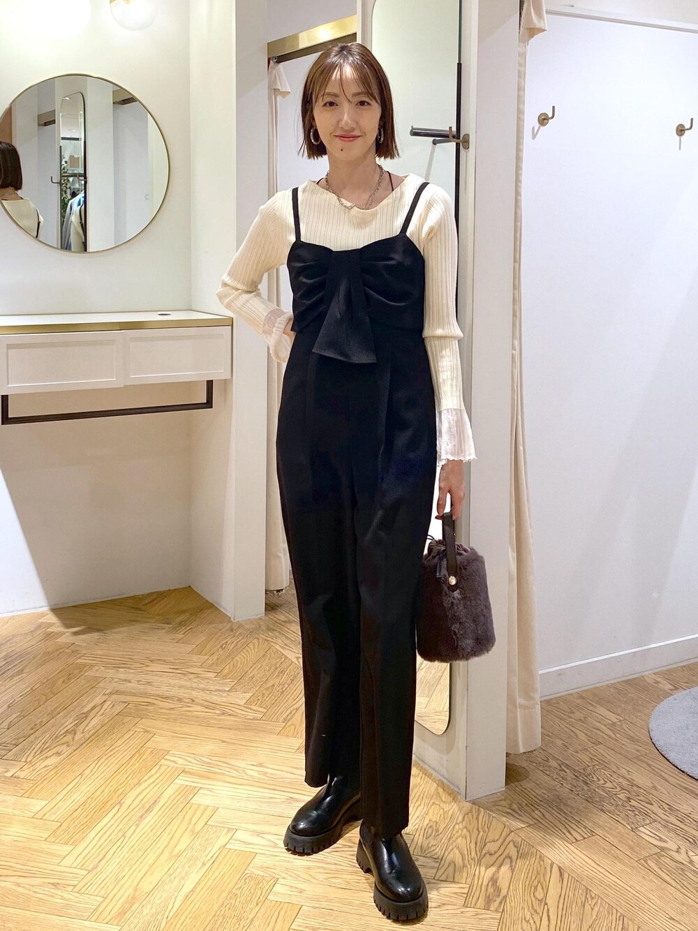 グレー系のショルダーバッグ、ブラック系のサロペット/オーバーオール、ホワイト系のニット/セーターを着用したレディースの冬コーディネートの1枚目の写真