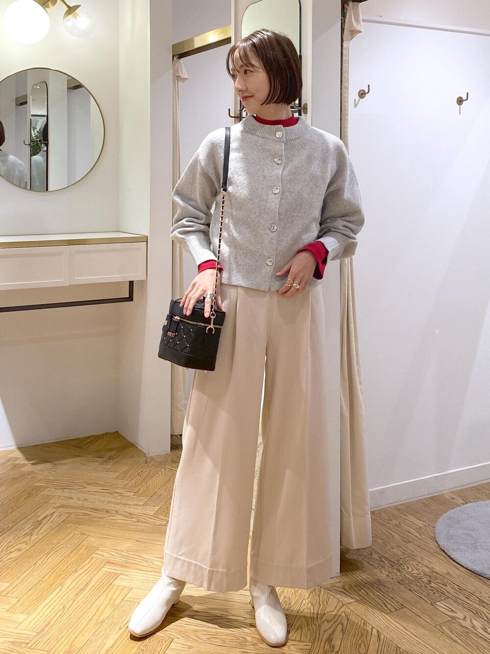 ホワイト系のブーツ、グレー系のカーディガン/ボレロ、レッド系のニット/セーターを着用したレディースの冬コーディネートの1枚目の写真