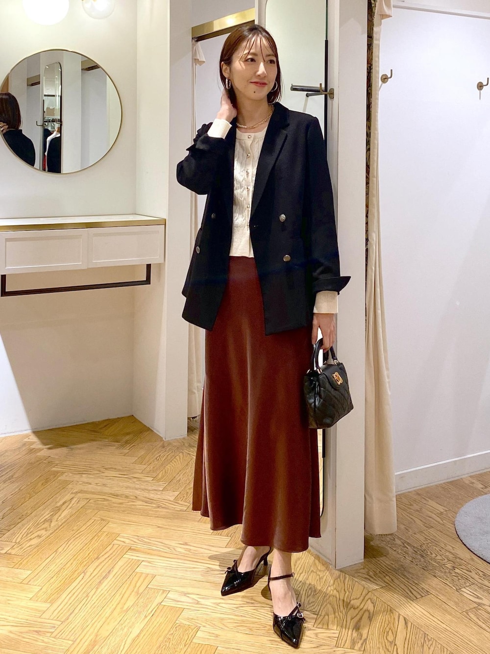 ブラック系のテーラードジャケット、ブラック系のパンプス、ブラウン系のスカートを着用したレディースの冬コーディネートの1枚目の写真