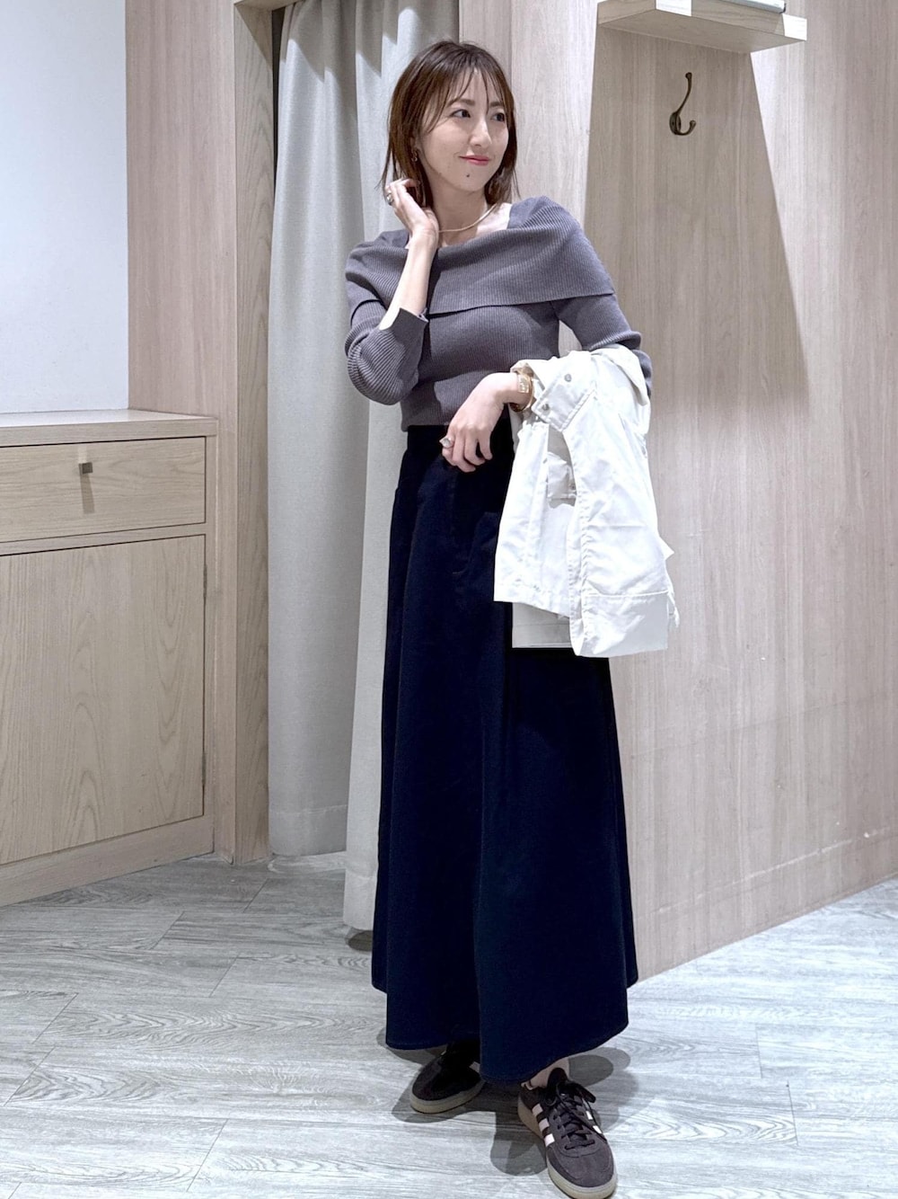 グレー系のニット/セーター、ブルー系のスカート、ホワイト系のナイロンジャケットを着用したレディースの春コーディネートの1枚目の写真