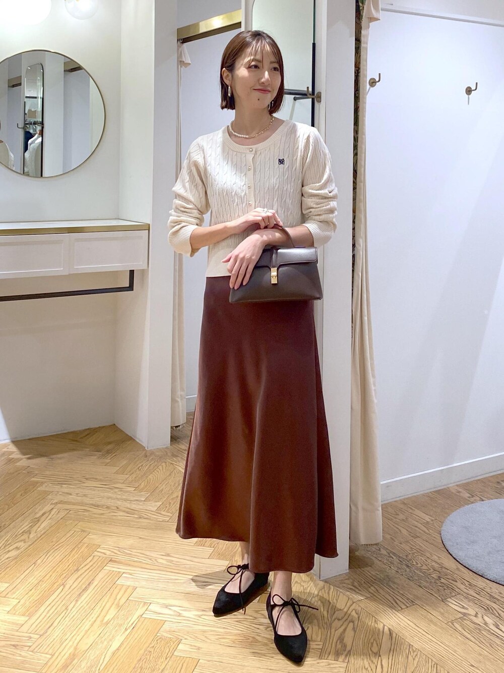 ブラウン系のスカート、ホワイト系のカーディガン/ボレロ、ブラック系のパンプスを着用したレディースの冬コーディネートの1枚目の写真