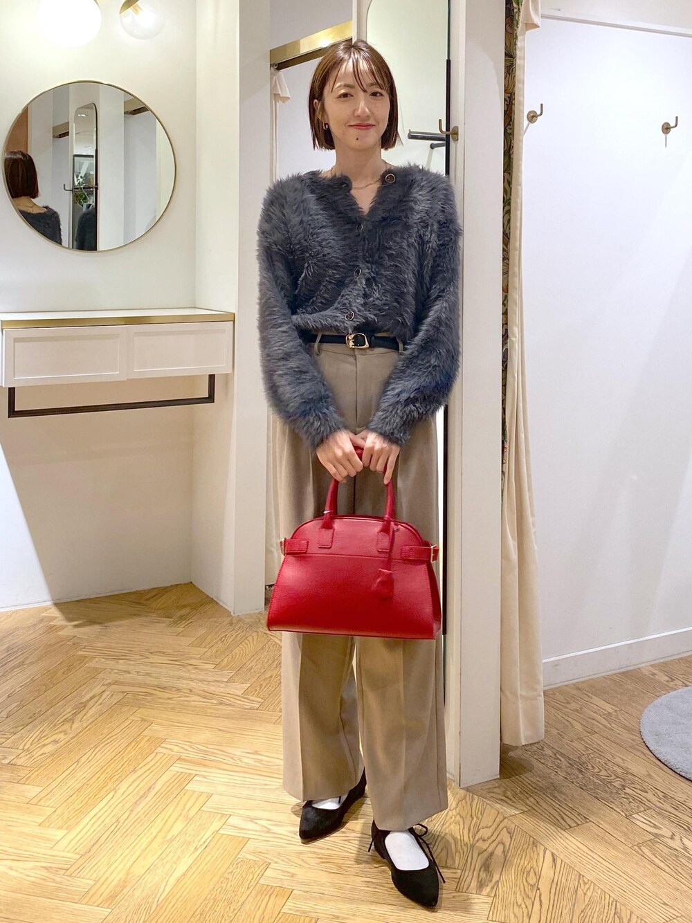レッド系のトートバッグ、ベージュ系のスラックス、グレー系のカーディガン/ボレロを着用したレディースの冬コーディネートの1枚目の写真