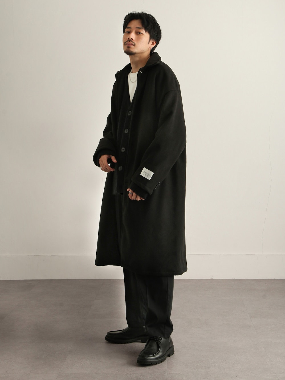 ブラック系のステンカラーコート、ブラック系のカーディガン/ボレロ、ブラック系のスラックスを着用したメンズの秋コーディネートの1枚目の写真