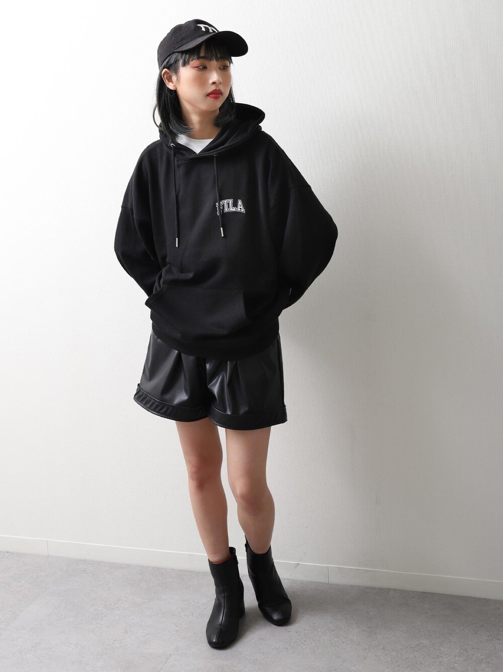 ブラック系のパーカー、ブラック系のブーツ、ブルー系のキャップを着用したレディースの冬コーディネートの1枚目の写真