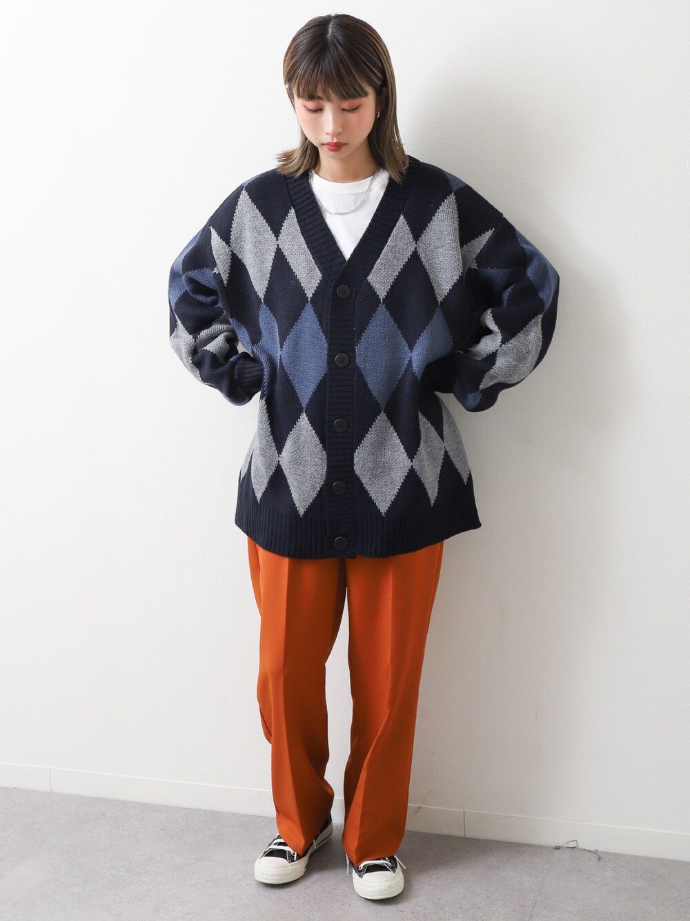 グレー系のカーディガン/ボレロ、オレンジ系のスラックス、ブラック系のスニーカーを着用したレディースの冬コーディネートの1枚目の写真