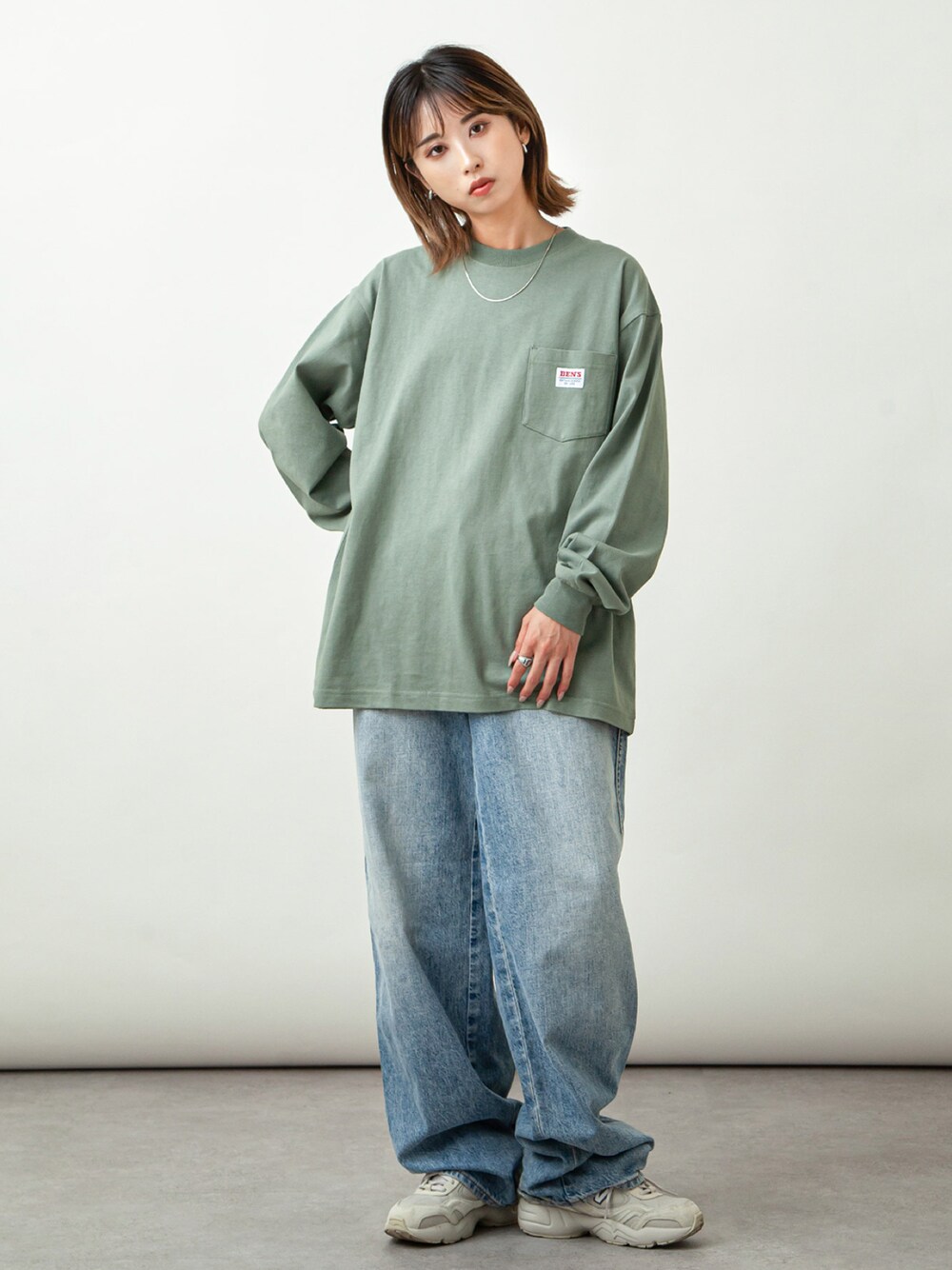 グリーン系のTシャツ/カットソー、ブルー系のデニムパンツ、ベージュ系のスニーカーを着用したレディースの秋コーディネートの1枚目の写真