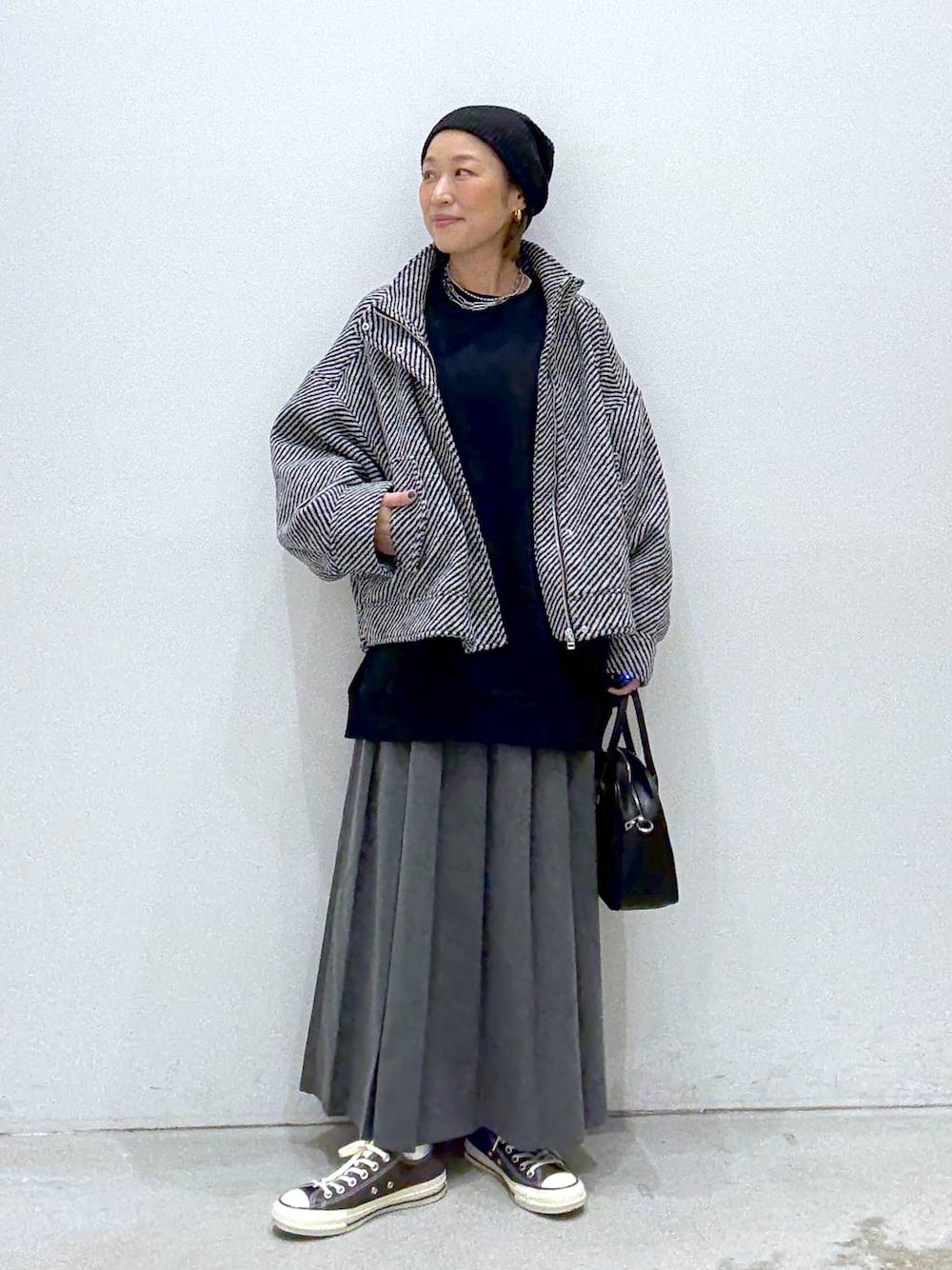 グレー系のスカート、ブラウン系のスニーカー、ブラック系のボストンバッグを着用したレディースの秋コーディネートの1枚目の写真