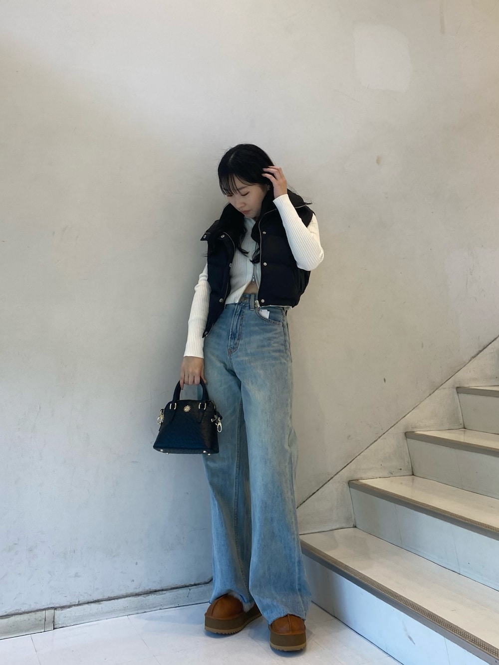 ブラック系のダウンベスト、ブルー系のデニムパンツ、ベージュ系のスリッポンを着用したレディースの秋コーディネートの1枚目の写真