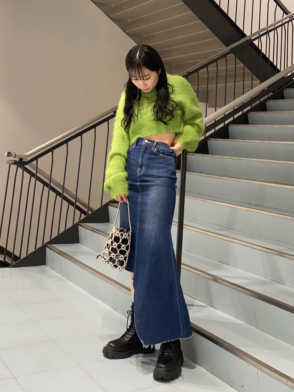 グリーン系のニット/セーター、ブルー系のデニムスカート、ブラック系のブーツを着用したレディースの冬コーディネートの1枚目の写真