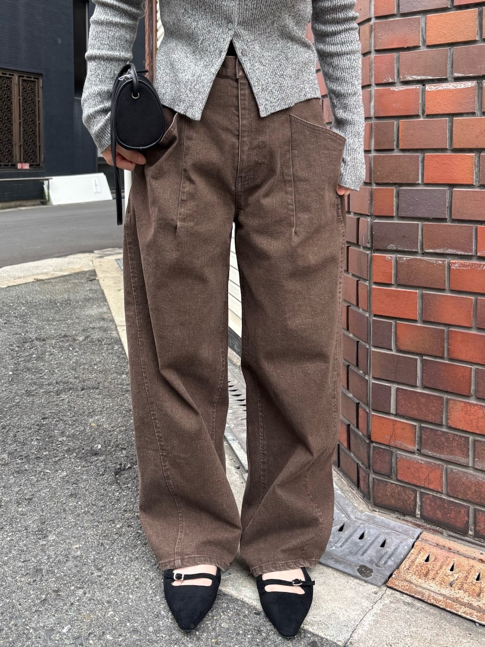 ブラウン系のデニムパンツ、グレー系のニット/セーター、ブラック系のショルダーバッグを着用したレディースの秋コーディネートの1枚目の写真