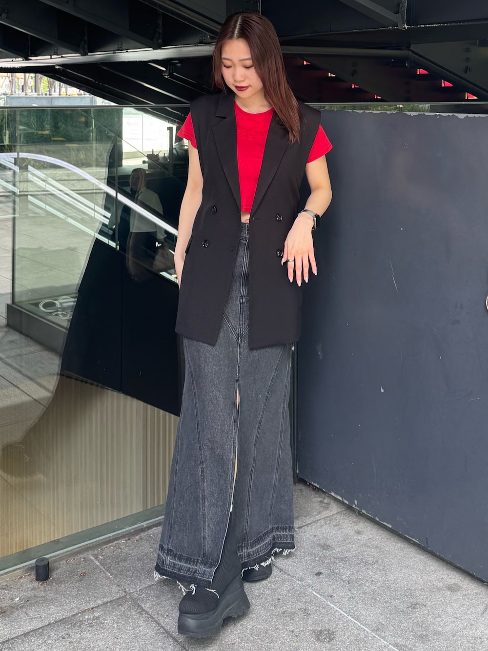 レッド系のTシャツ/カットソー、ブラック系のベスト、ブラック系のデニムスカートを着用したレディースの春コーディネートの1枚目の写真