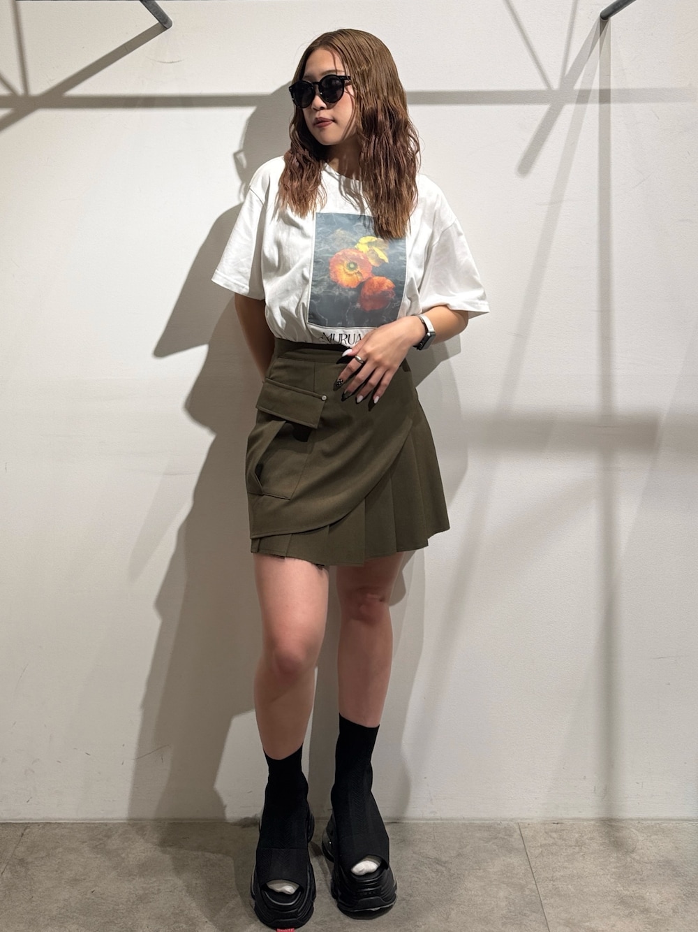 グリーン系のスカート、ホワイト系のTシャツ/カットソー、ブラック系のサンダルを着用したレディースの夏コーディネートの1枚目の写真