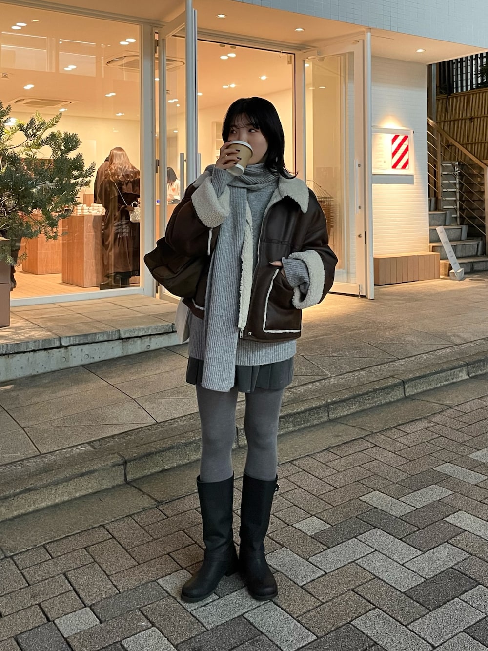 ブラウン系のムートンコート、グレー系のニット/セーター、ブラウン系のショルダーバッグを着用したレディースの冬コーディネートの1枚目の写真
