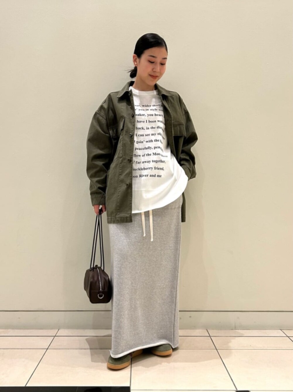 グレー系のスカート、ホワイト系のTシャツ/カットソー、グリーン系のミリタリージャケットを着用したレディースの冬コーディネートの1枚目の写真