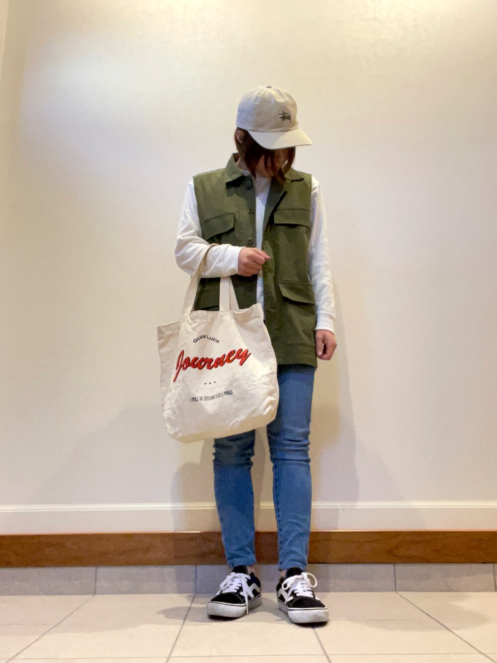 グリーン系のベスト、ホワイト系のトートバッグ、ブルー系のデニムパンツを着用したレディースの秋コーディネートの1枚目の写真
