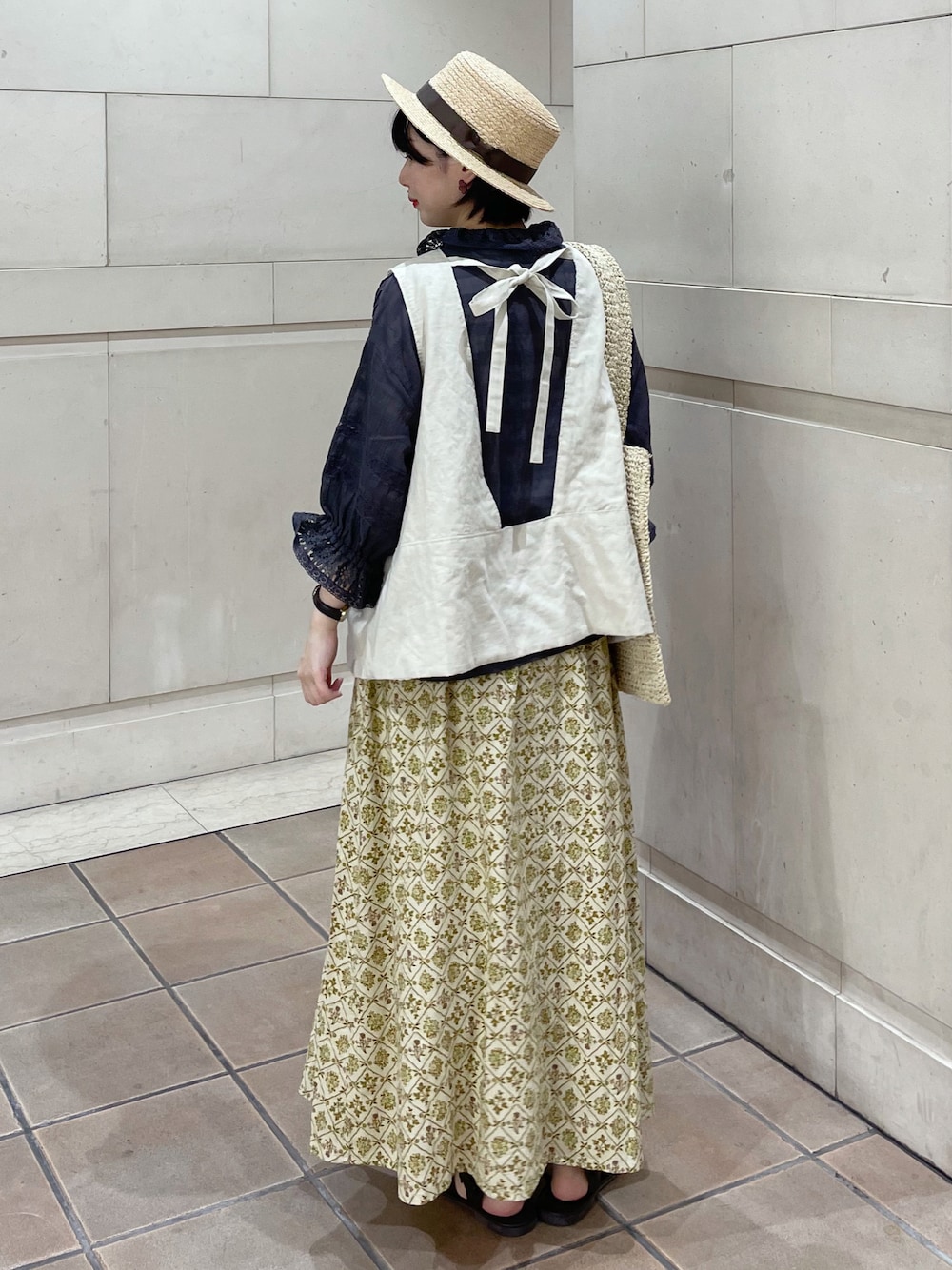ブラウン系のサンダル、ベージュ系のスカート、ホワイト系のベストを着用したレディースの春コーディネートの1枚目の写真