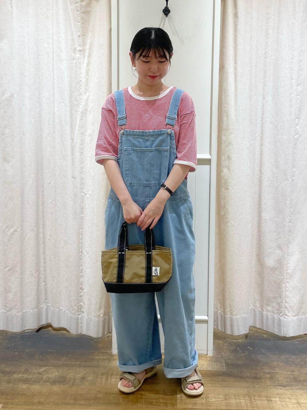 レッド系のTシャツ/カットソー、ブルー系のサロペット/オーバーオール、ベージュ系のハンドバッグを着用したレディースの冬コーディネートの1枚目の写真