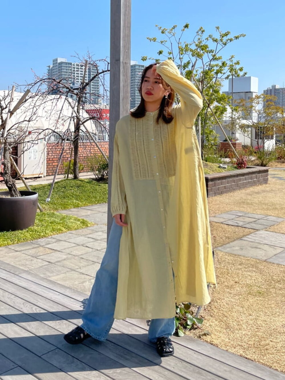 イエロー系のワンピース、ブラック系のサンダル、ブルー系のデニムパンツを着用したレディースの春コーディネートの1枚目の写真