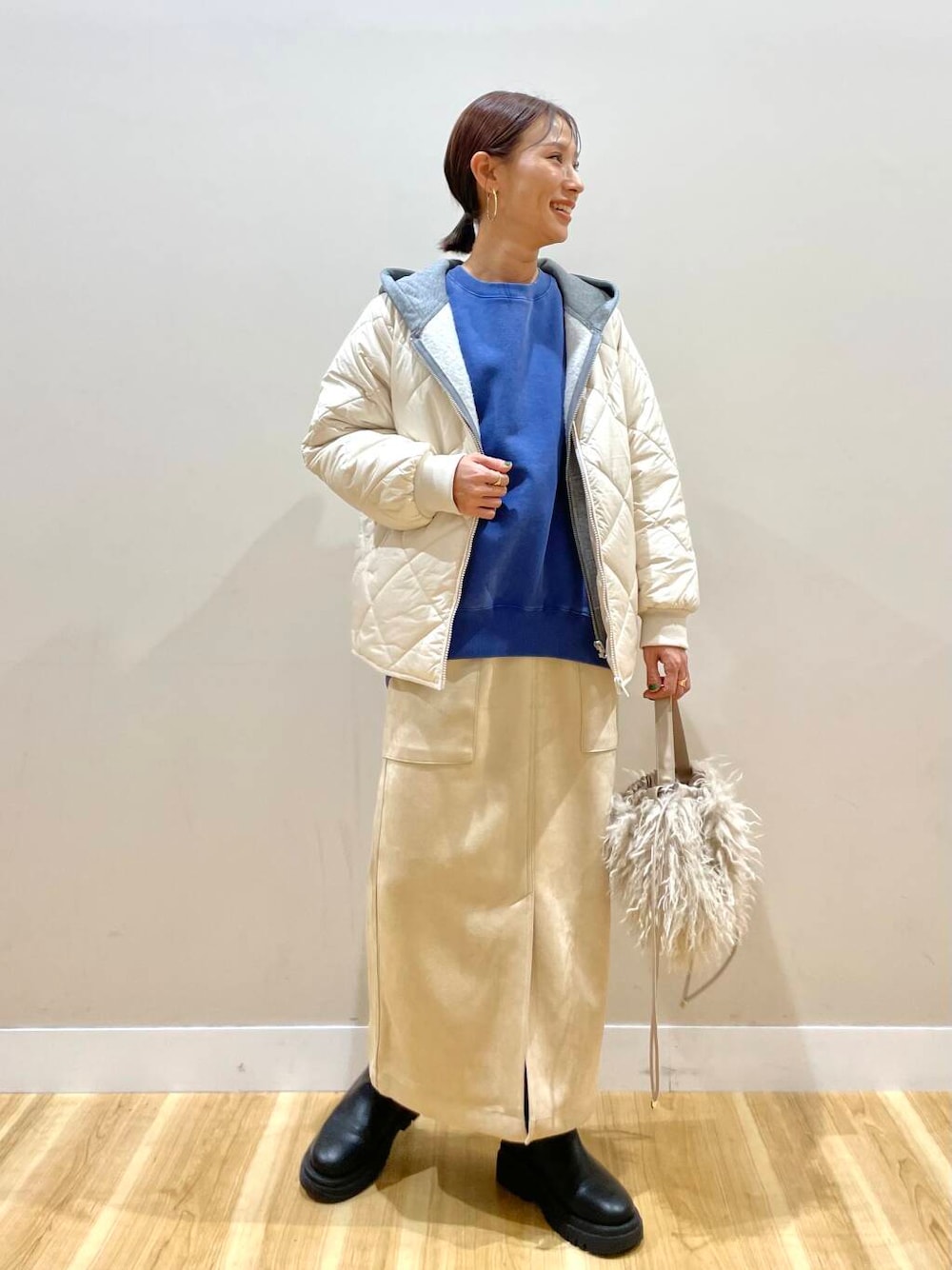 ベージュ系のショルダーバッグ、ホワイト系のスカート、グレー系のパーカーを着用したレディースの冬コーディネートの1枚目の写真