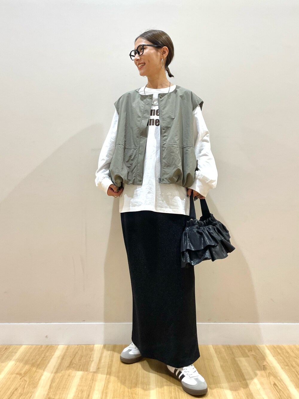 グリーン系のベスト、ホワイト系のTシャツ/カットソー、ブラック系のスカートを着用したレディースの秋コーディネートの1枚目の写真