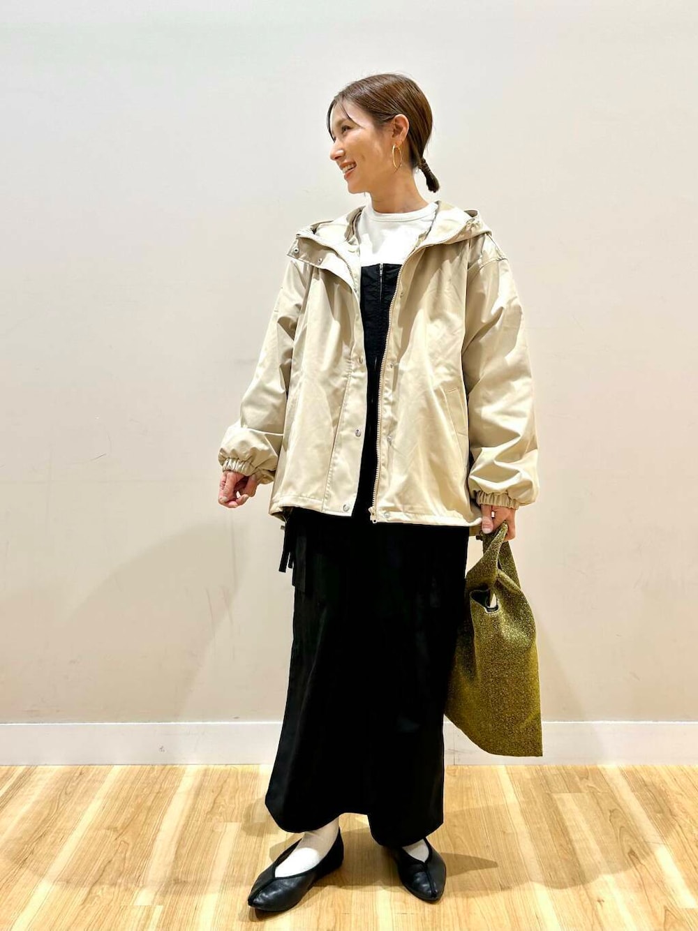 ゴールド系のトートバッグ、ベージュ系のマウンテンパーカー、ホワイト系のスウェットを着用したレディースの冬コーディネートの1枚目の写真